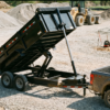Black 7x14 tandem-axle dump trailer with hydraulic bed raised on a gravel job site — dump trailers for sale at PrimeLoad