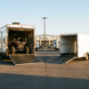 Side-by-side comparison of a white toy hauler RV with rear ramp down beside a plain V-nose enclosed cargo trailer — toy hauler vs enclosed cargo at PrimeLoad