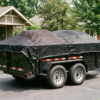 Black 6x12 utility trailer loaded with mulch and topsoil under a heavy-duty mesh tarp on a residential driveway — how to tarp a utility trailer at PrimeLoad