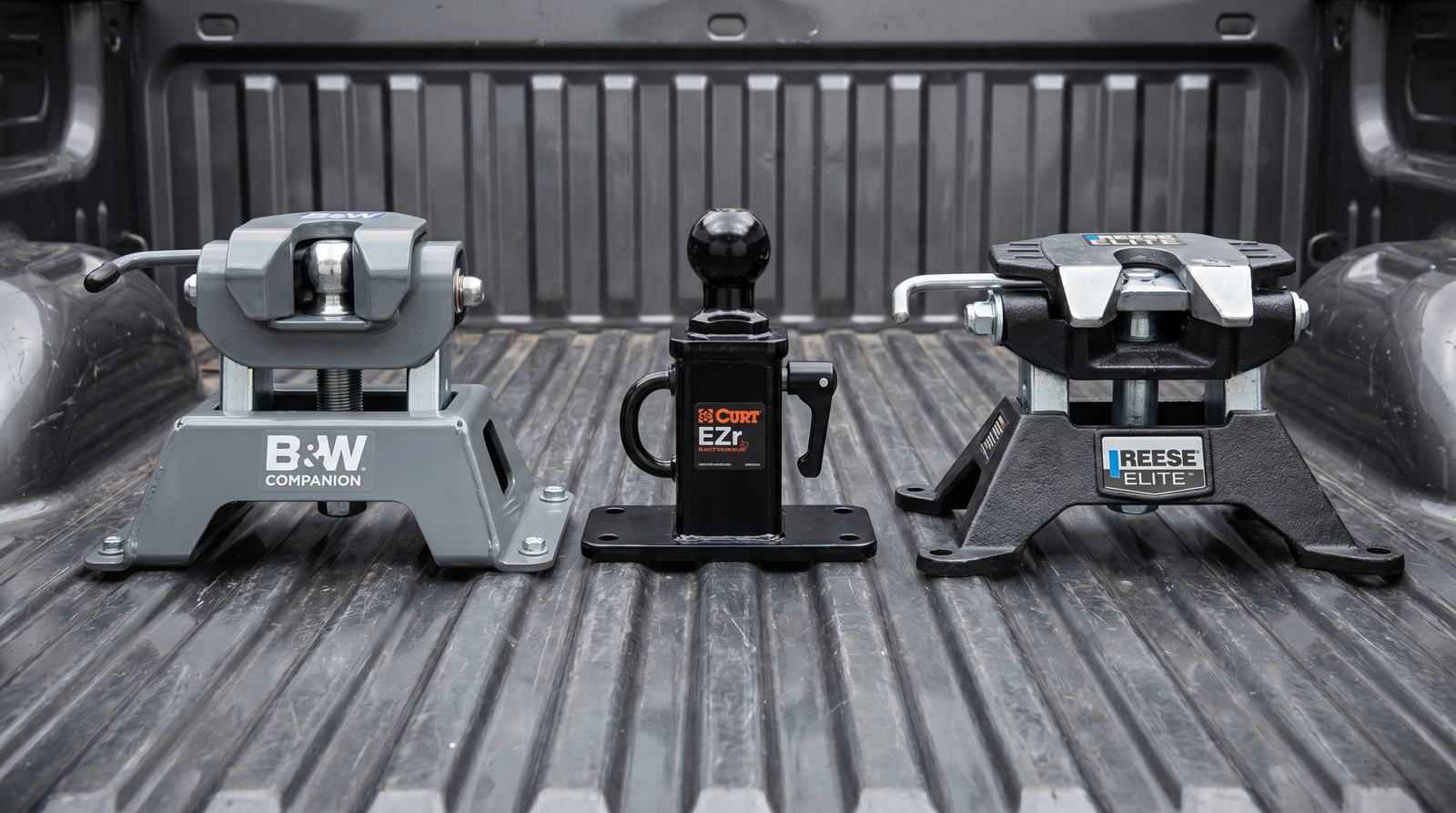 Three gooseneck hitch ball assemblies side-by-side: B&W Companion, Curt EZr, Reese ELITE in a pickup bed — gooseneck hitch comparison at PrimeLoad
