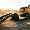 Black detachable gooseneck lowboy trailer with deck lowered to the ground and an excavator parked on it — detachable lowboy trailer at PrimeLoad